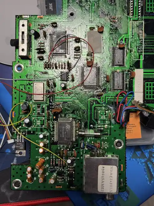 A close-up photo of a heavily damaged green circuit board with melted solder, burnt components, and wires taped haphazardly…