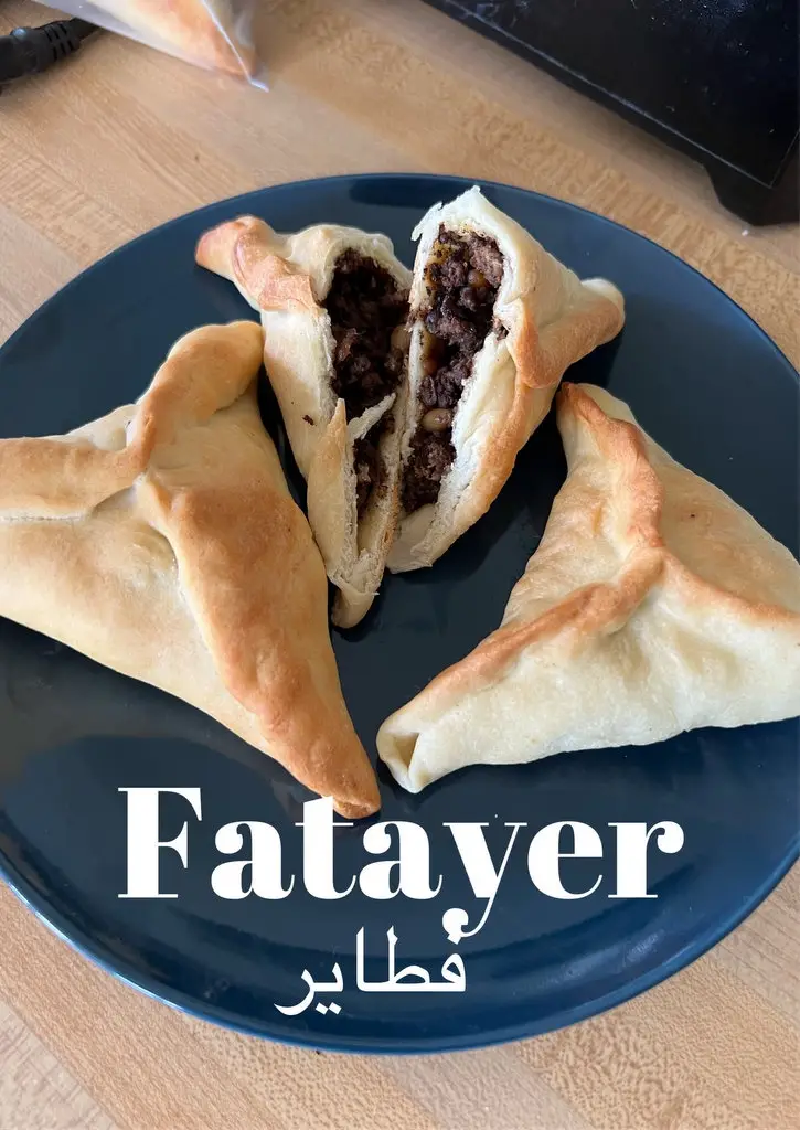 A dark blue plate holds three golden-brown, triangular pastries, one split open to reveal a savory meat and bean filling…