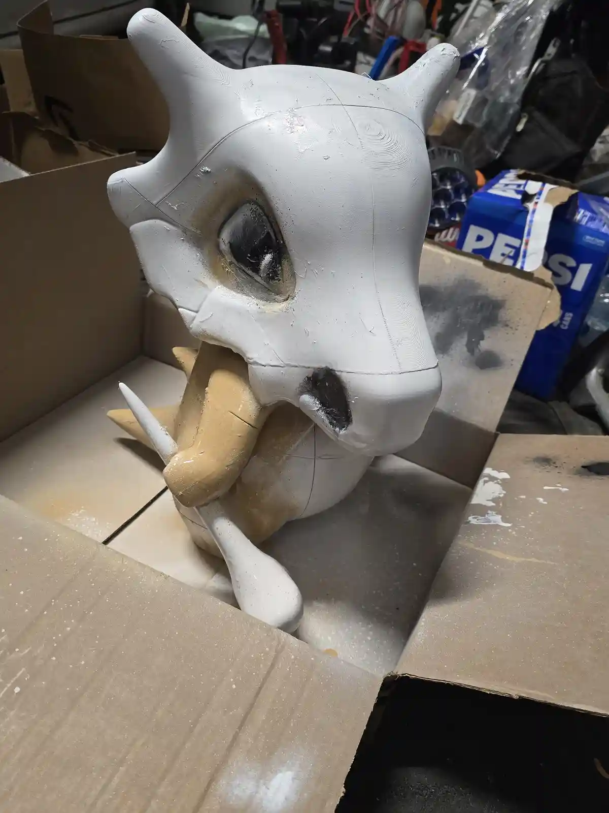 A partially painted, unfinished 3D-printed Dragonite head sculpture sits in a cardboard box, showing visible spray-paint…
