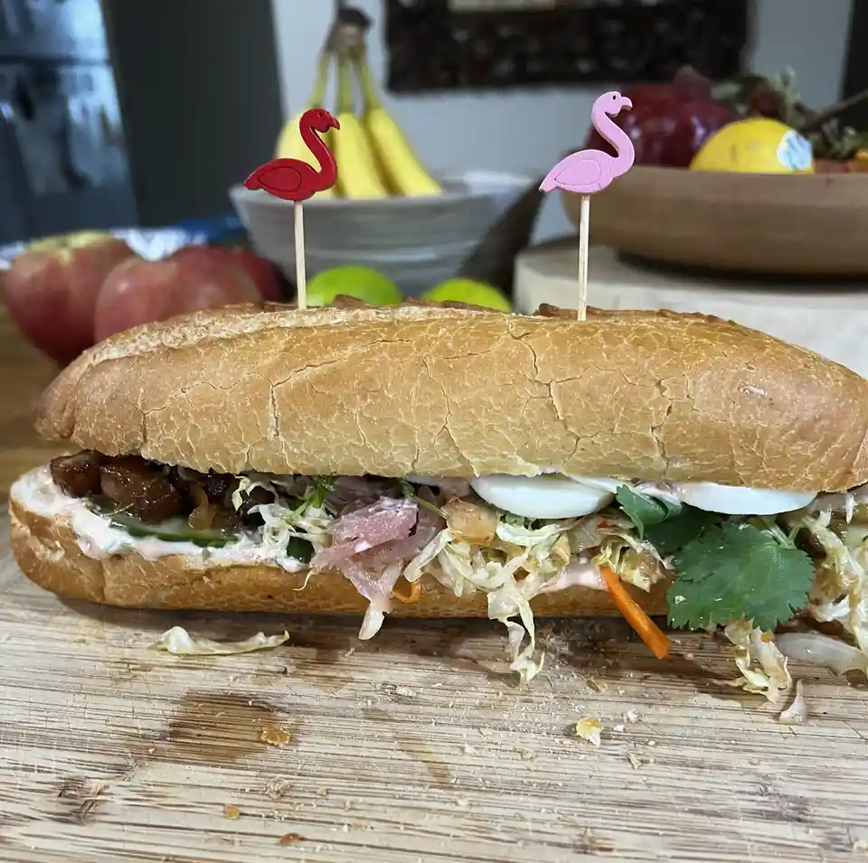 A close-up photo of a long sandwich on a wooden cutting board, filled with various ingredients including shredded cabbage…