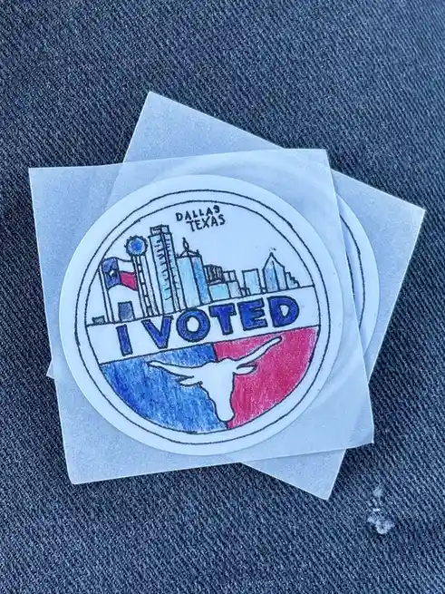 A close-up photo shows several circular 'I VOTED' stickers from Dallas, Texas, resting on a denim surface. The sticker…