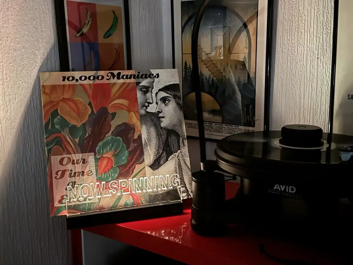 A vinyl record album cover for '10,000 Maniacs - Our Time An Edge' is displayed on a red shelf next to a black AVID…