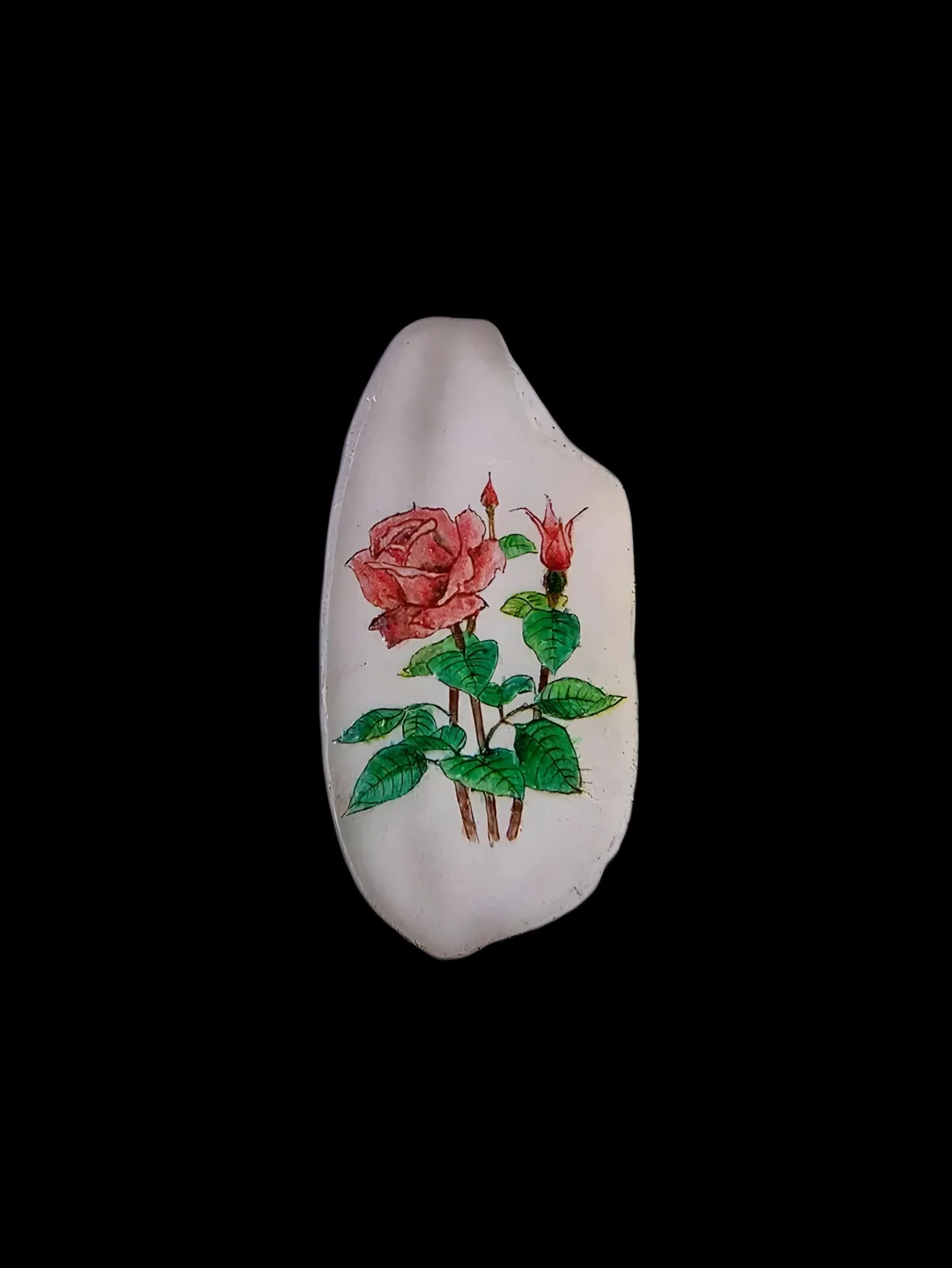 A white, irregularly shaped stone with a hand-painted illustration of a pink rose in bloom and a smaller red rosebud…
