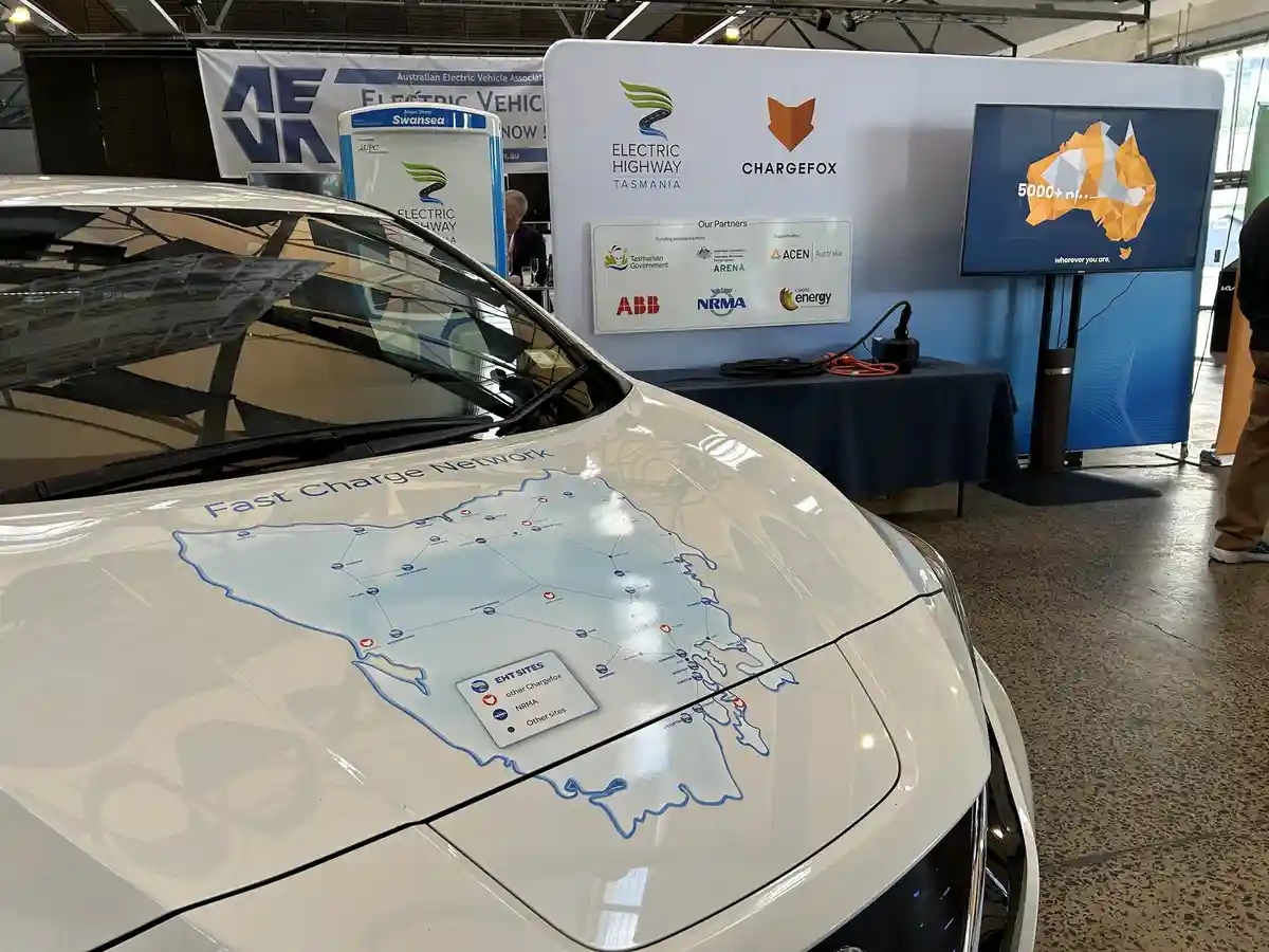 A white electric car has a map of Tasmania printed on its hood showing a 'Fast Charge Network' with various charging station…