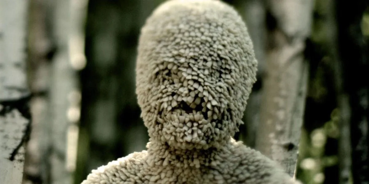 A close-up shot of a humanoid figure covered entirely in dense, shaggy, light-colored wool or sheepskin, obscuring all…