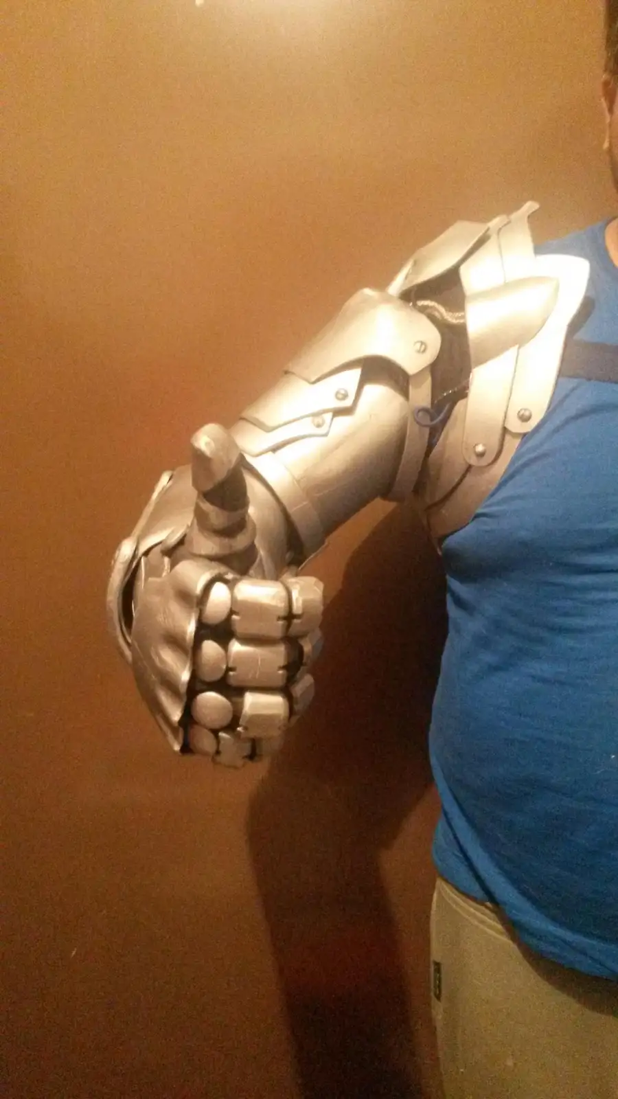 A person wearing a blue t-shirt and beige pants has their right arm covered in silver-colored, articulated medieval-style…