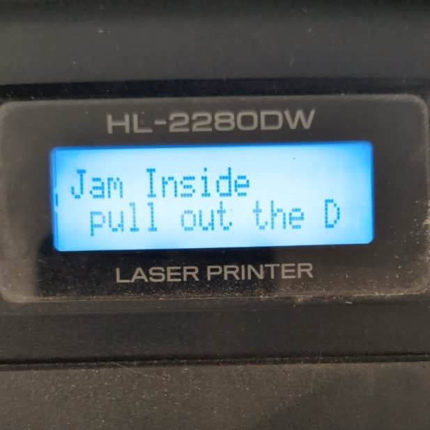 A close-up of a black HP Laser Printer's LCD screen displaying the error message 'Jam Inside pull out the D' in pixelated…