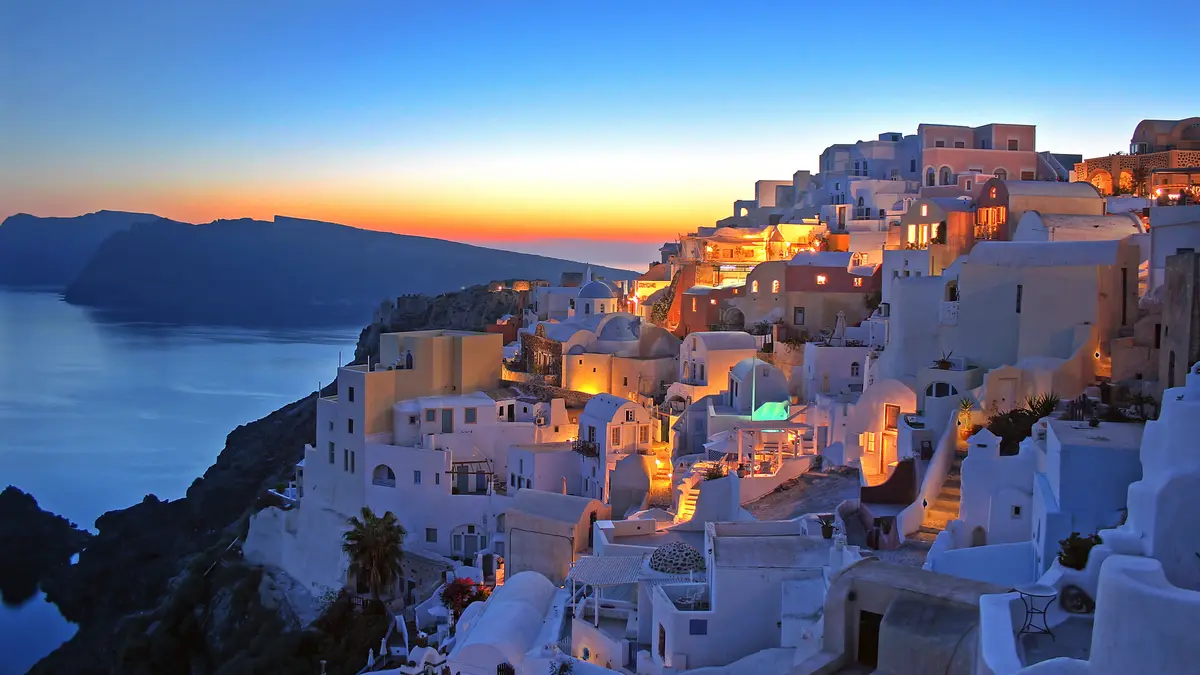 In Oia, Santorini's main town, pink-hued twilight bathes the whitewashed buildings cascading down steep hills, as the…