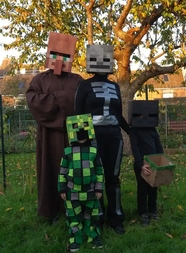 Four people dressed as Minecraft characters — a brown-robed Steve, a black-and-silver Steve, a green Creeper, and a child…