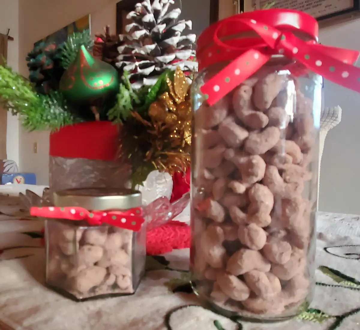 Two glass jars filled with chocolate-covered peanuts sit on a table, each tied with a red polka-dot ribbon. Behind them is a…