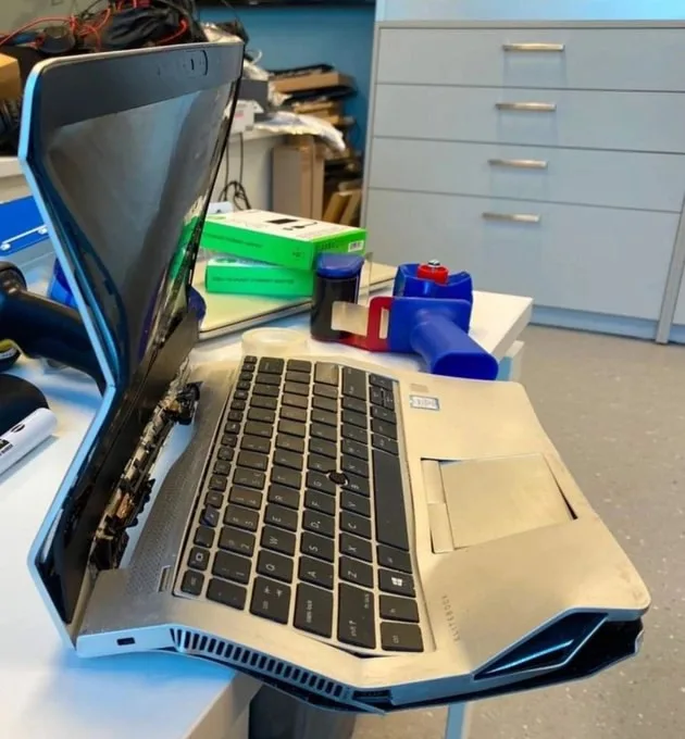 A silver laptop is shown on a desk with its back panel removed, exposing internal components and wiring. The laptop is…