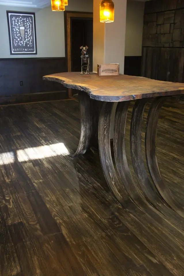 a large, rustic wooden table with thick, curved legs stands in a room with dark hardwood floors. The legs visibly sag and…
