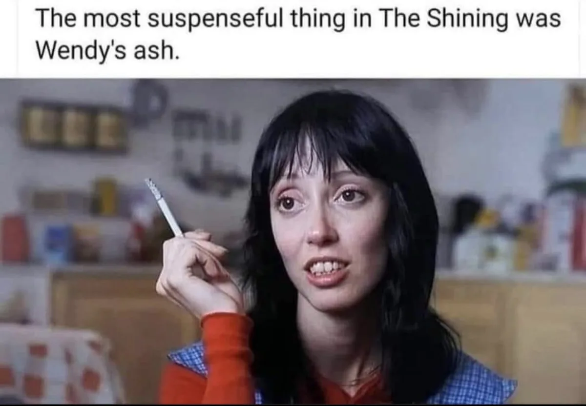 A still image of Wendy Torrance from the movie 'The Shining' holding a cigarette with a shocked or alarmed expression. The…