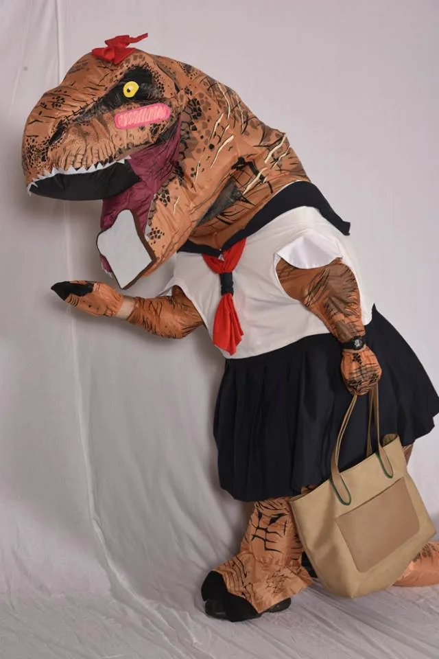 A person in a full-body inflatable T-Rex costume is dressed in a Japanese schoolgirl uniform, complete with a white sailor…