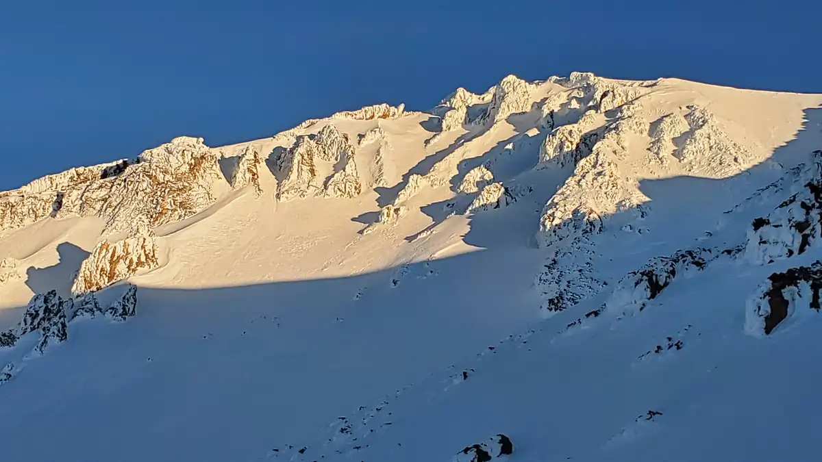 A majestic snow-covered mountain range under a clear blue sky, with sunlight highlighting the ridges and casting long…