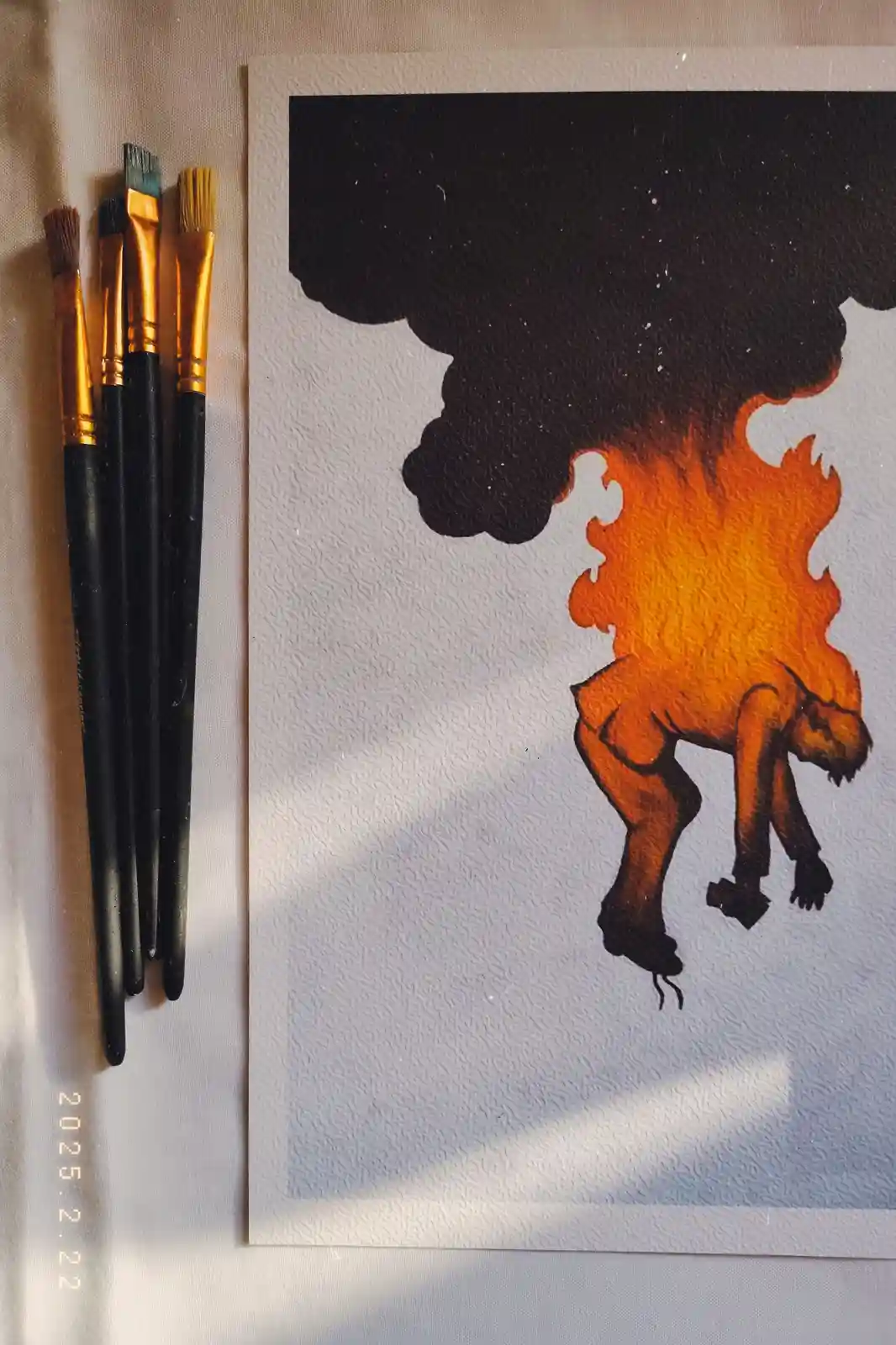 A painting depicts a figure engulfed in flames with smoke rising above, placed next to four paintbrushes on a textured…