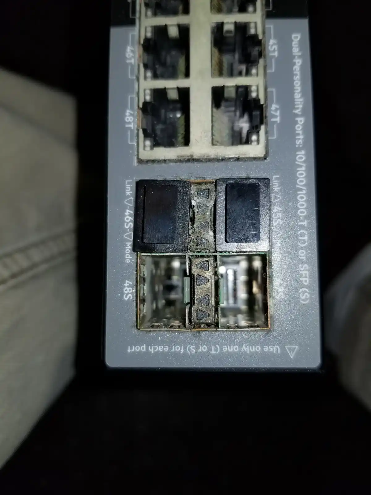 A close-up photo of a network switch's port section shows two adjacent ports with their protective plastic covers broken off…