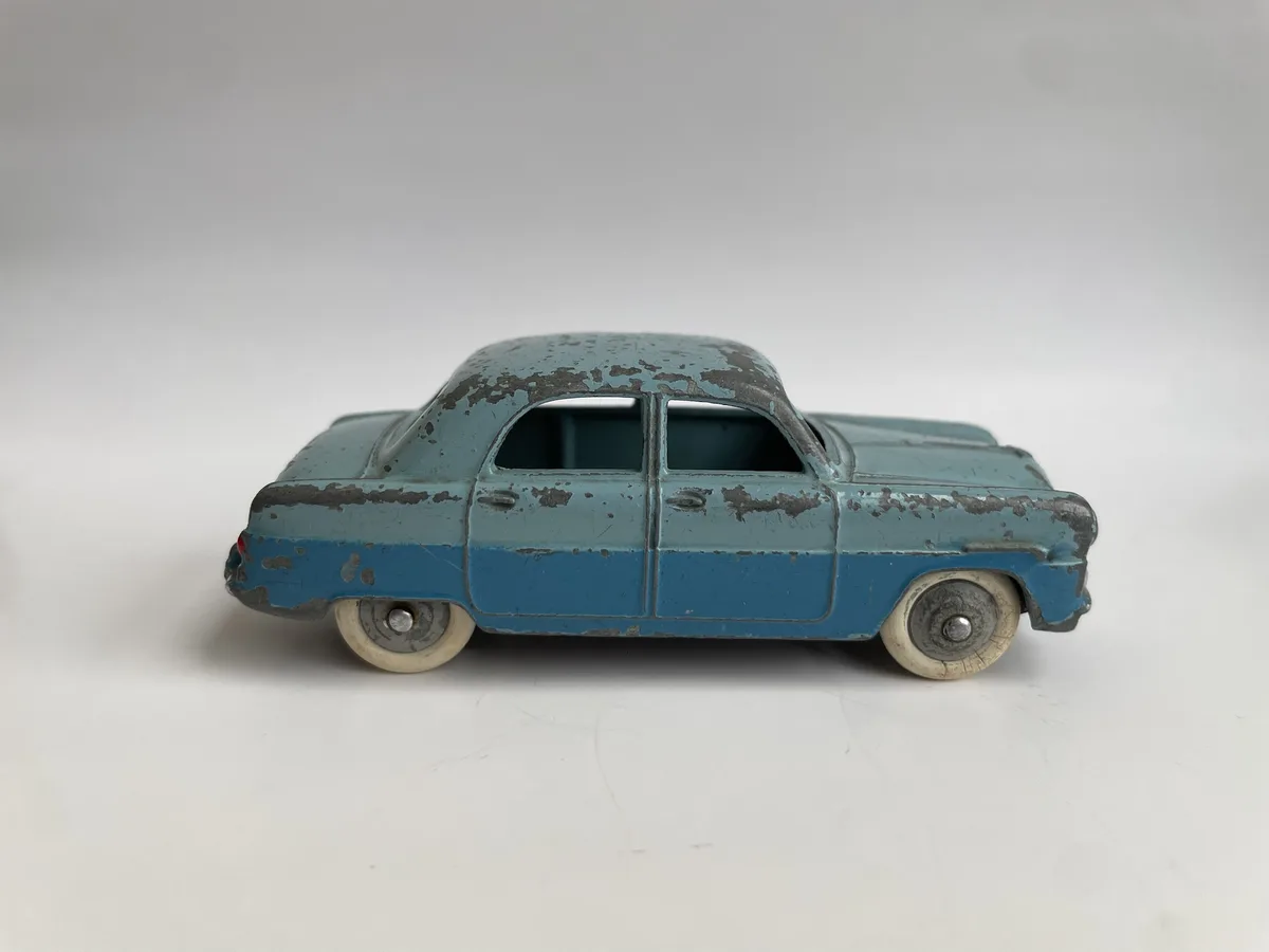 A weathered, two-tone blue vintage toy car with chipped paint and visible rust, photographed against a plain white…