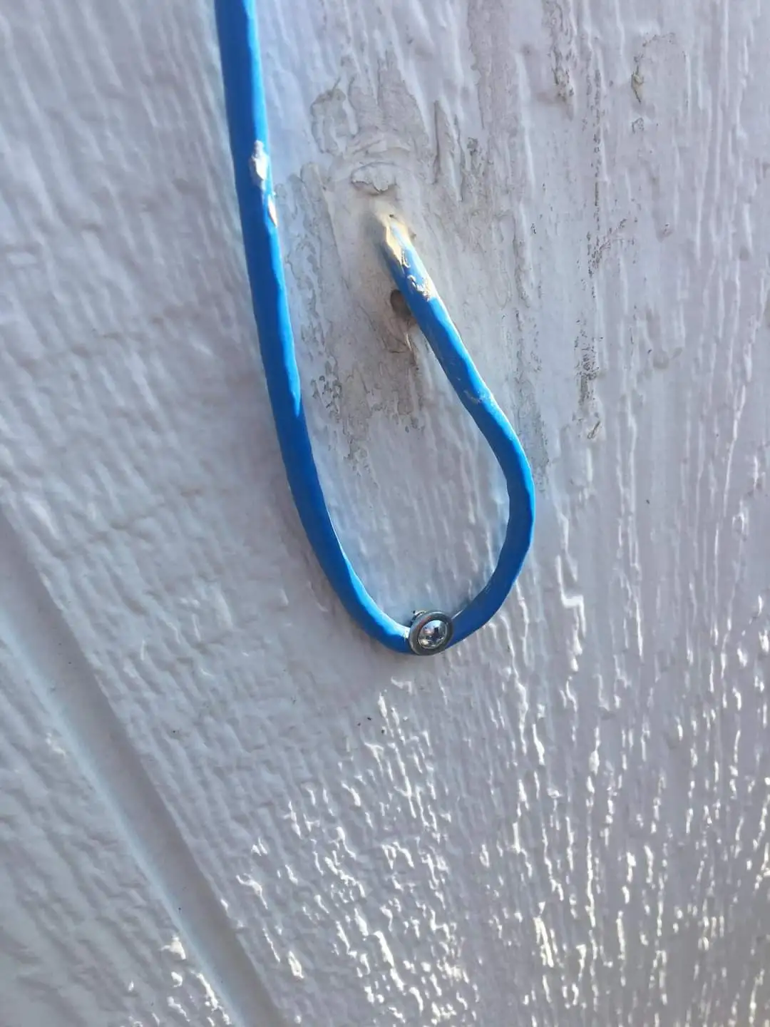 A blue cable is looped around a screw on a white, textured wall, forming a shape resembling a ring. The overlaid text reads…