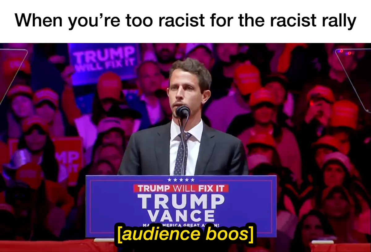 A man in a suit stands at a podium with 'TRUMP WILL FIX IT' and 'TRUMP VANCE' written on it, addressing a crowd wearing red…