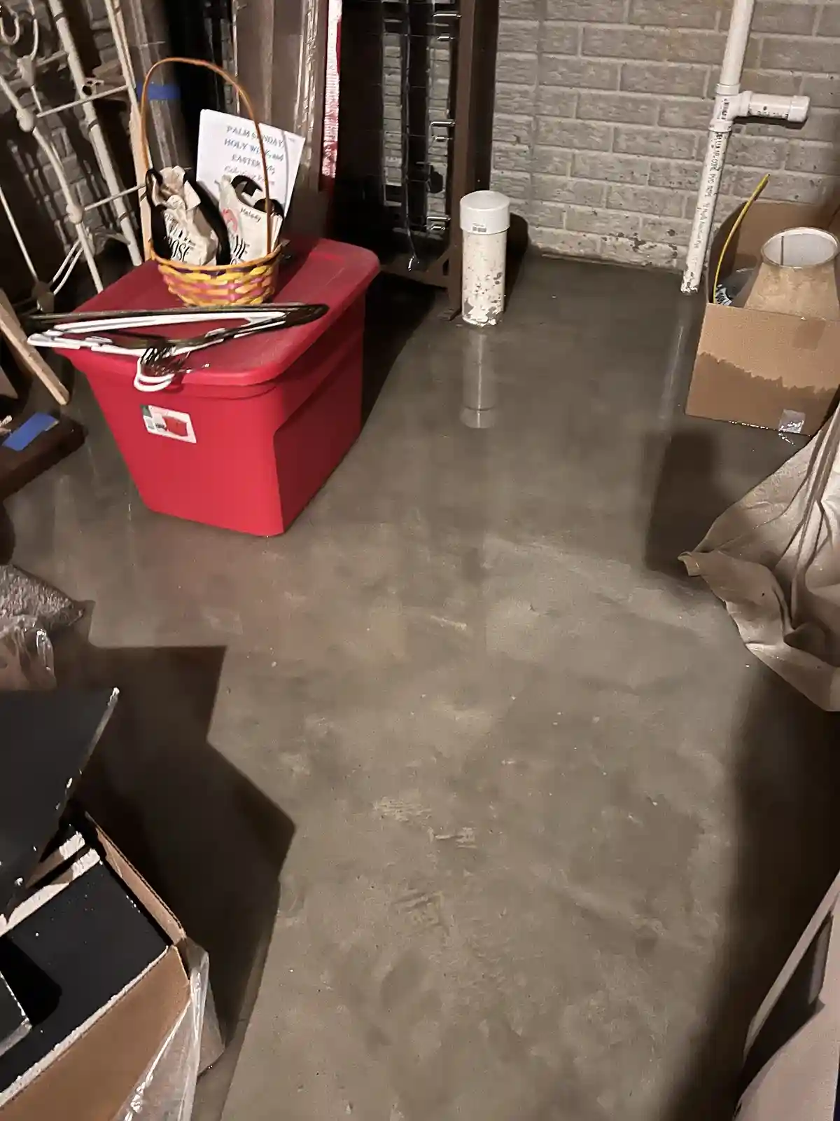 A photo of a cluttered garage floor with a red storage bin, cardboard boxes, and various items scattered around. The…