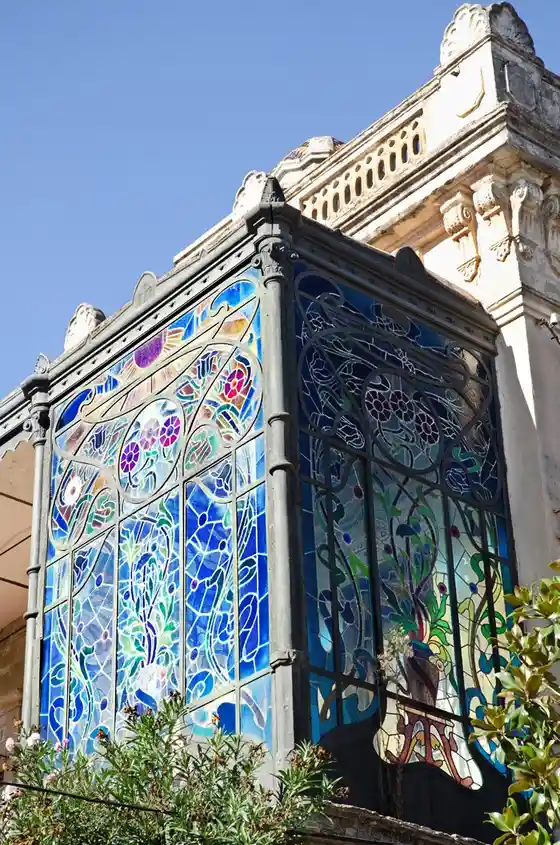 a photograph of an ornate, colorful stained glass window with floral and abstract patterns set in dark metal framing…