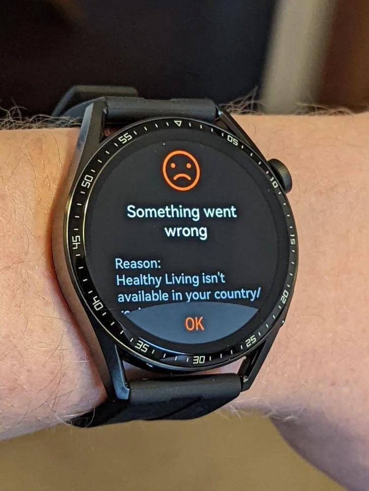 A close-up of a smartwatch on a person's wrist displaying an error message with an orange sad face icon. The text reads…