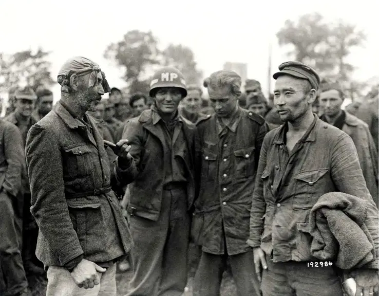 A black-and-white historical photo shows a group of soldiers, including one with an 'MP' helmet, confronting a man in…