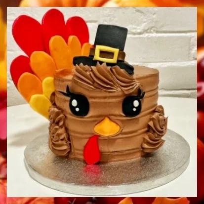 A round chocolate cake decorated to resemble a cartoon turkey with large black eyes, an orange beak, and a red wattle. It…