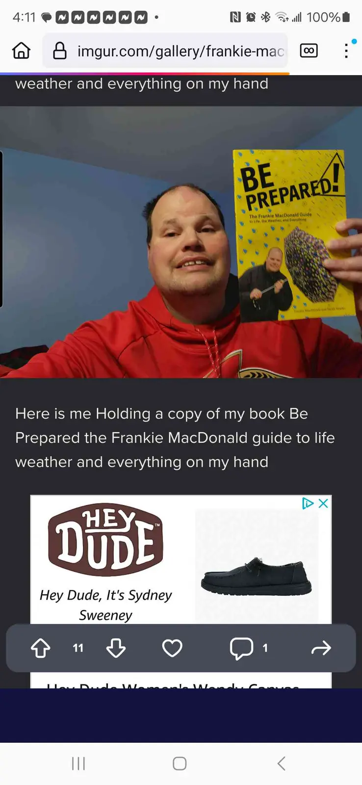 A man in a red hoodie holds up a yellow book titled 'BE PREPARED! The Frankie MacDonald Guide to Life, the Weather and…