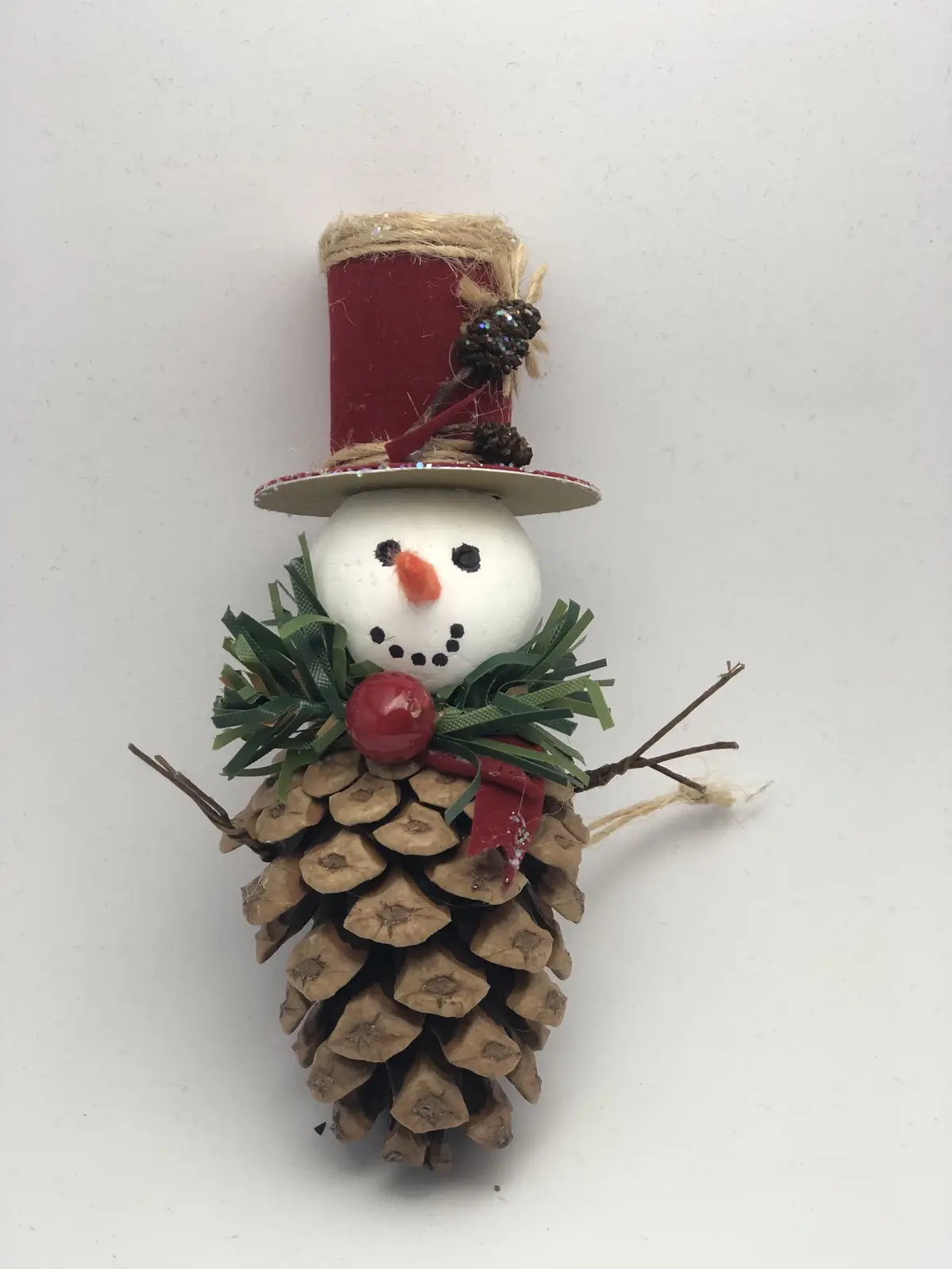A handmade Christmas decoration shaped like a snowman, constructed from a pinecone body, a white painted egg for a head, a…