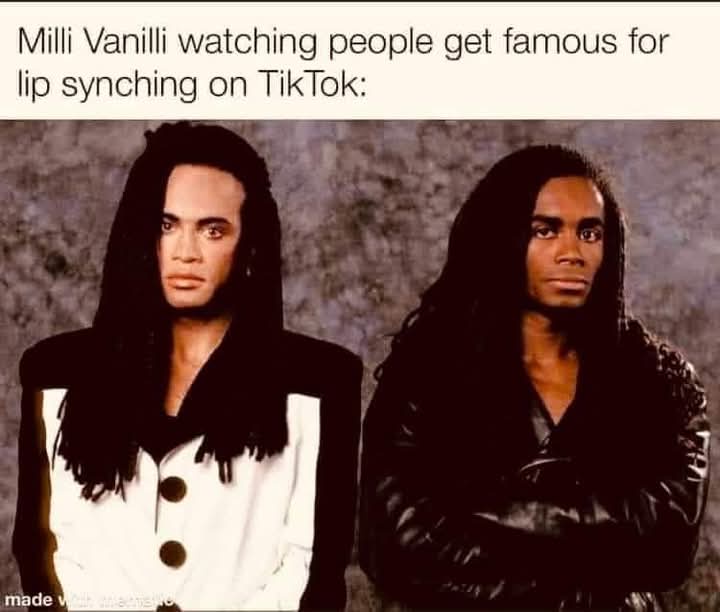 The image shows two men, identified as Milli Vanilli, with long dark hair, looking intensely at the camera. The man on the…