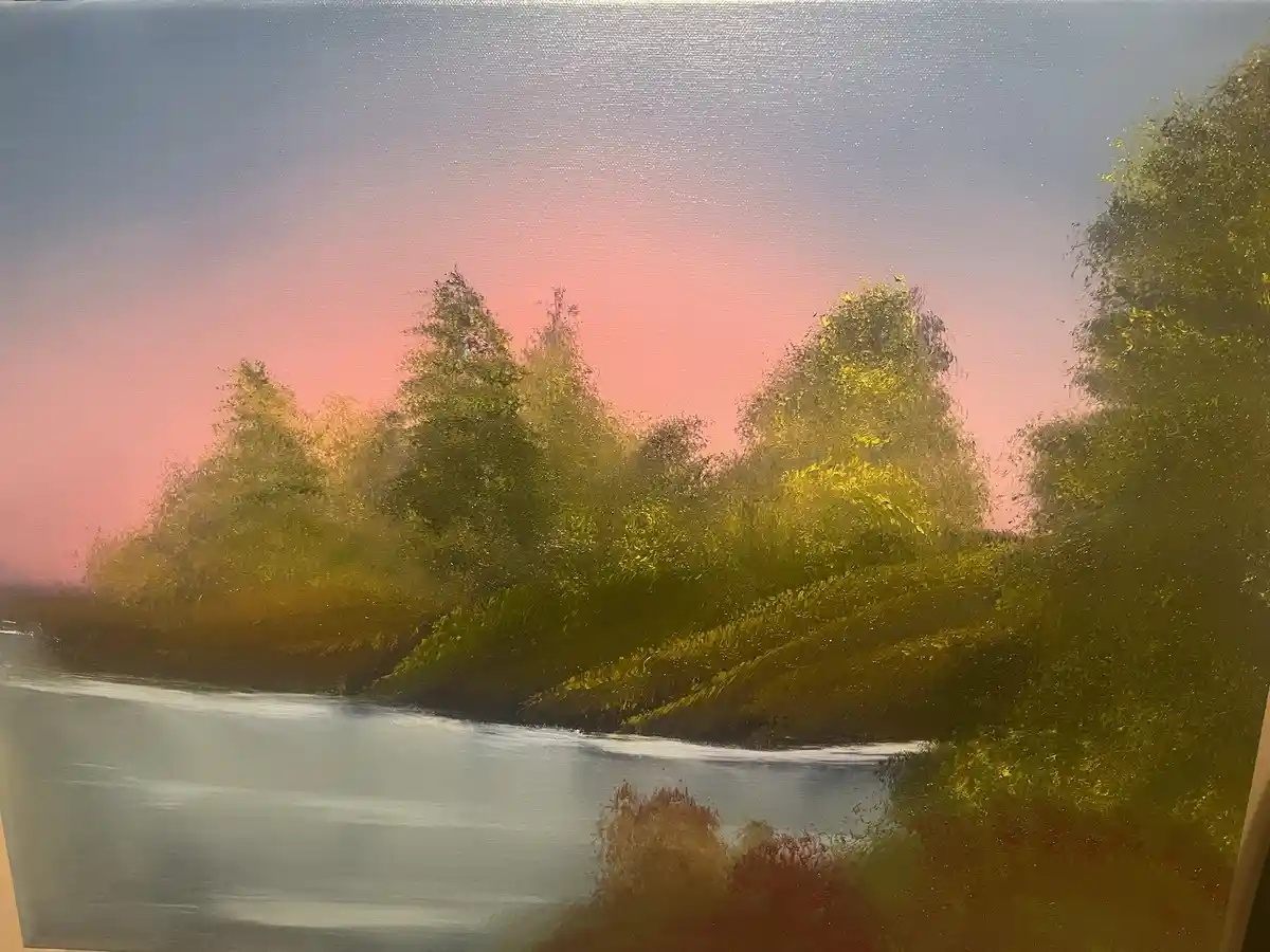 A painting depicts a serene river scene at sunset, with pink and blue skies reflected in calm water, surrounded by green…