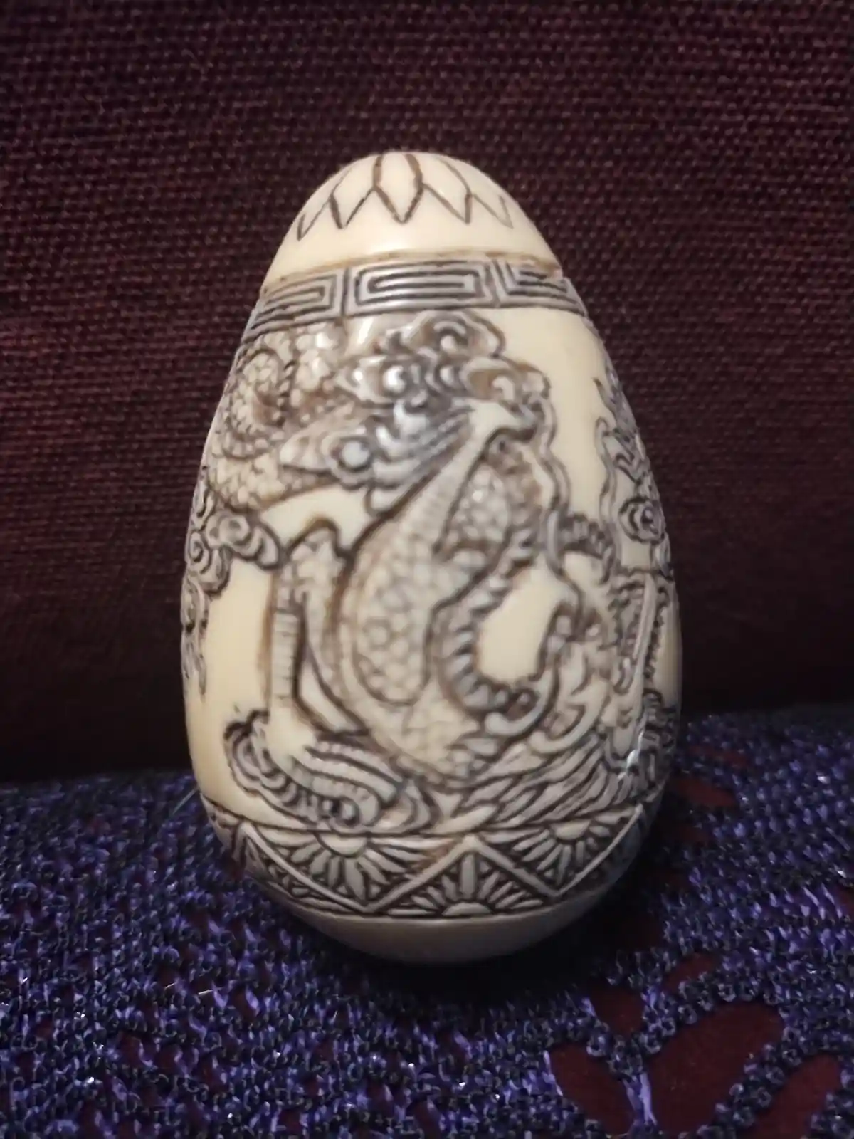 a close-up photo shows an intricately carved, off-white, egg-shaped object with a detailed dragon design etched into its…