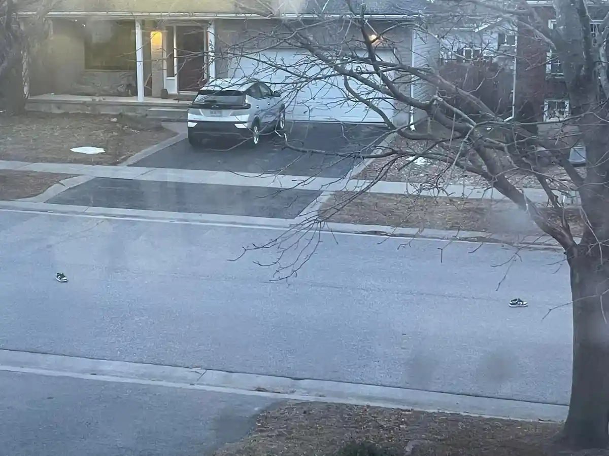 A residential street view shows a silver SUV parked in a driveway in front of a house with a garage. Two black-and-white…