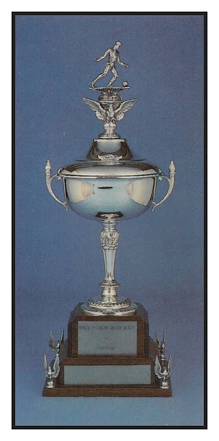 A silver trophy with a footballer statue on top, standing on a wooden base engraved with 'WORLD CUP IN SOCCER HISTORY' and…