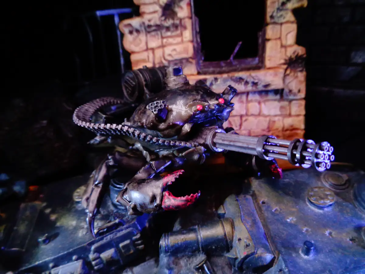 A heavily detailed, darkly painted miniature of a biomechanical, crab-like war machine with glowing red eyes and a…