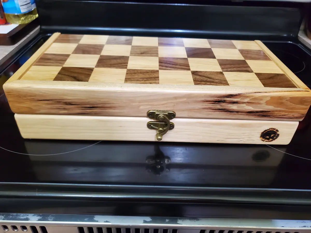 A wooden chessboard with alternating light and dark squares is shown resting on a black electric stove top. The board has a…