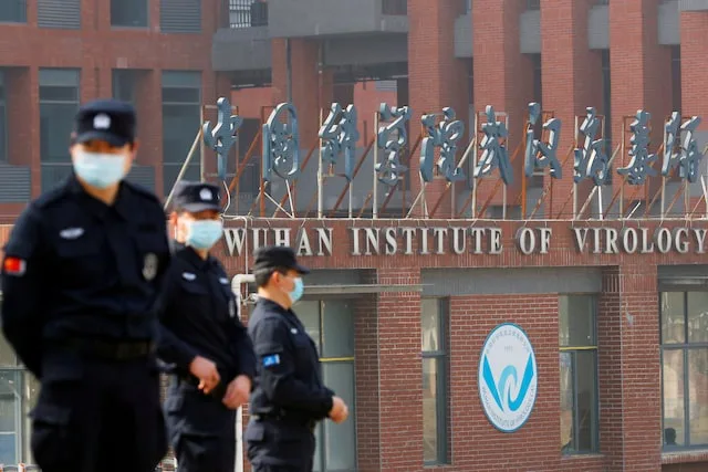 Three uniformed security guards wearing face masks walk in front of a brick building with a large sign reading…