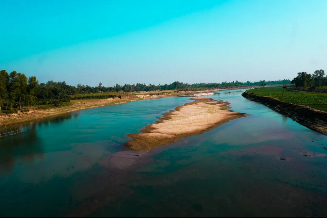 A wide river with turquoise water flows through a landscape with green fields and trees on both banks, featuring a prominent…