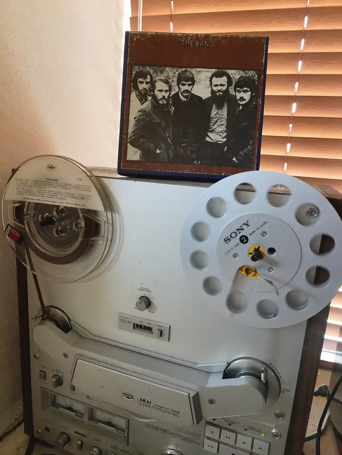 A vintage Akai reel-to-reel tape recorder with a Sony reel on the right and an Ampex reel on the left, has a worn album…