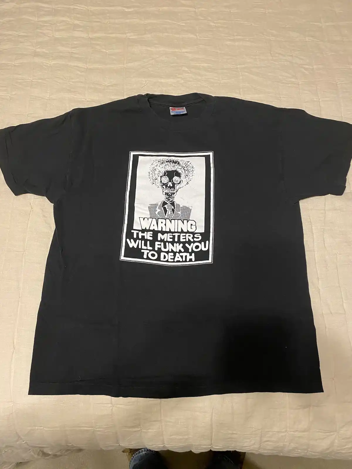 A black t-shirt laid flat on a light-colored bedspread features a white rectangular graphic. The graphic shows a stylized…