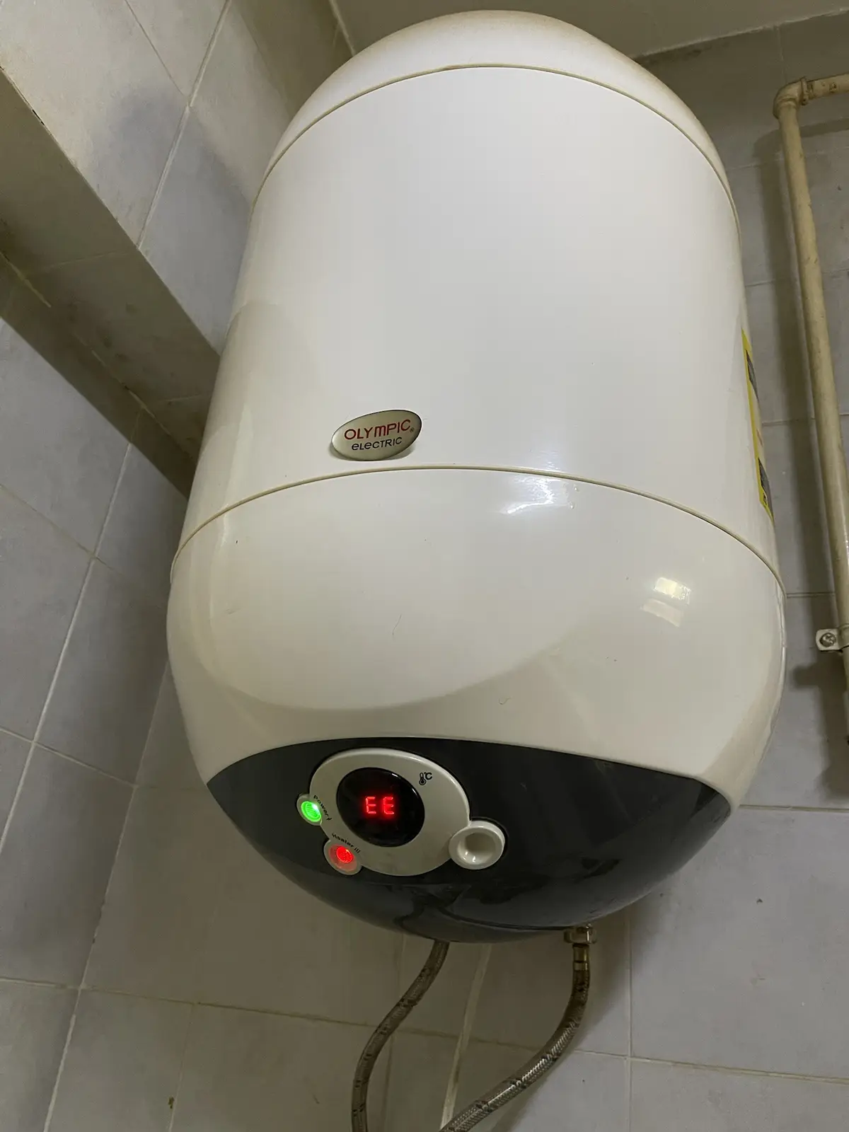 A white Olympic Electric water heater mounted on tiled walls shows a red digital display reading 'EE' with a green power…