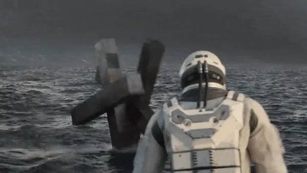 A person in a white spacesuit stands in water, facing a large black letter 'X' that slowly rotates to reveal the letter 'K'…