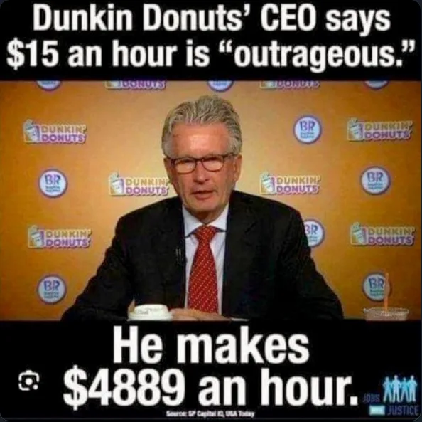 A man in a suit and glasses sits at a table in front of a Dunkin' Donuts branded backdrop. The text at the top reads 'Dunkin…