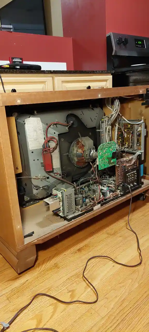 A disassembled television sits on a wooden stand with its internal components exposed, including circuit boards, wires, and…