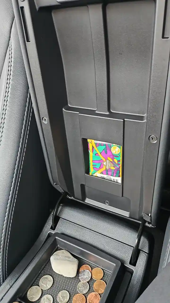 A close-up photo shows the inside of a car's center console, where a small compartment holds a large, smooth rock alongside…