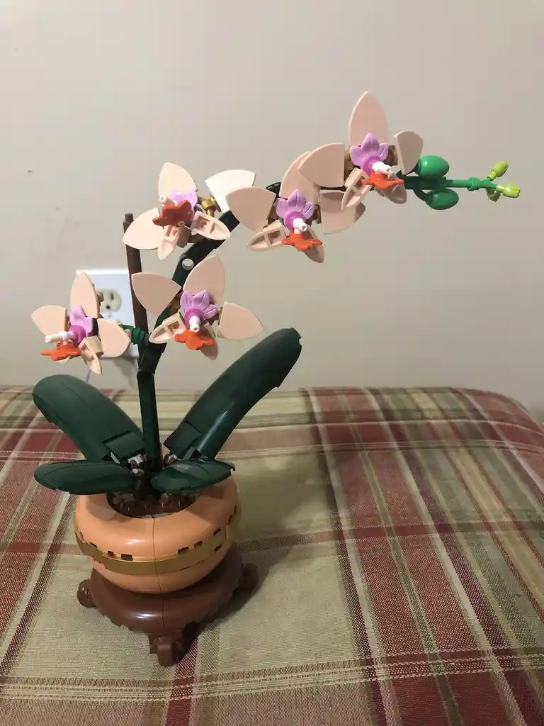 A detailed LEGO model of an orchid plant with pink and purple flowers, green stems and leaves, and a terracotta pot, sitting…