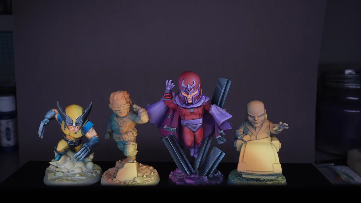 Four chibi-style Marvel figurines are displayed on a shelf: Wolverine with claws extended, Cyclops with his visor on…