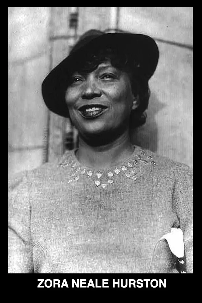 A black-and-white photograph shows Zora Neale Hurston smiling warmly while wearing a dark hat and a light-colored top with a…